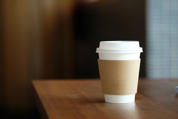 A disposable paper coffee cup sits on a wooden table