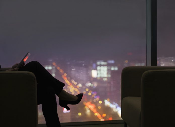 Business woman sits in front of glass window showing city at night