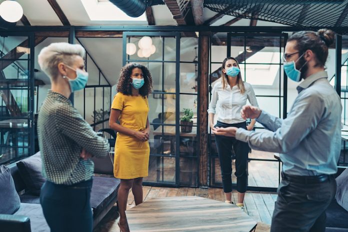 Four people wearing face masks meet in-person while social distancing