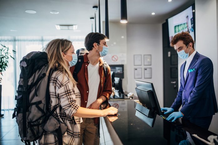 Two guests check in at a hotel during the COVID-19 pandemic wearing face masks