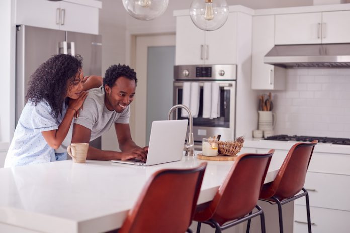 A couple at home uses a laptop to shop for a hotel and make travel plans.