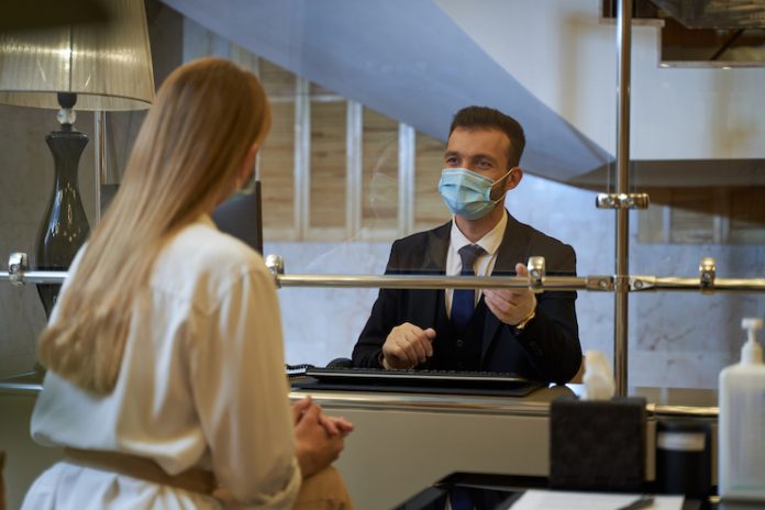 Hotel front-desk staff member checking in a guest while wearing a face mask