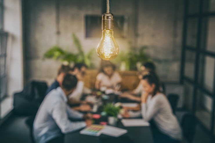 Group of people meet with lightbulb in foreground, signifying innovation