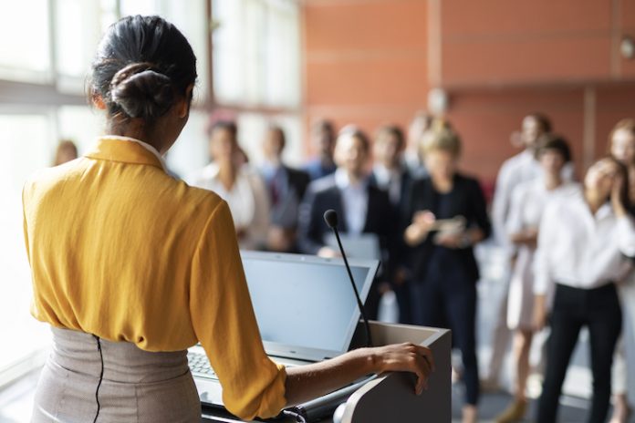 Women stands at a podium and addresses audience